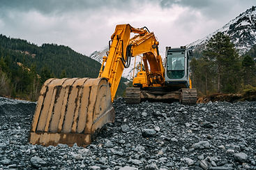 Yellow construction digger on rocky terrain with mountains and trees in the background