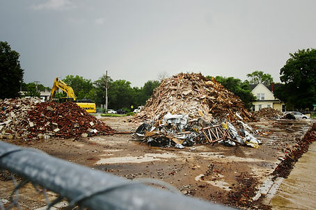 Piles of construction waste including wood and bricks. A yellow digger can be seen moving waste in the background