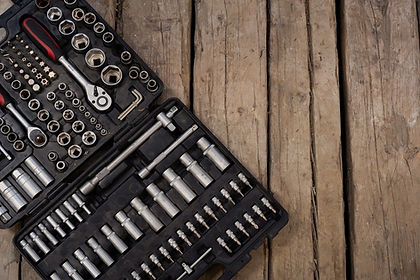 An open black toolbox containing a variety of tools. The toolbox is open flat against a rustic wooden plank background.