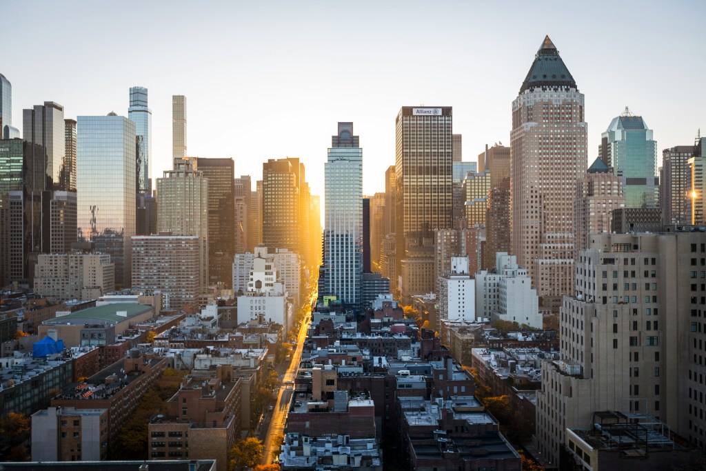 City landscape consisting of tall buildings, with setting sun shining through the gaps